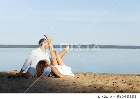 Happy international couple lying on beach. Caucasian man kisses Latin woman's leg. Laughing female, happy male enjoy romantic trip, celebrating honeymoon, St Valentine Day. Horizontal, copy space 98548181