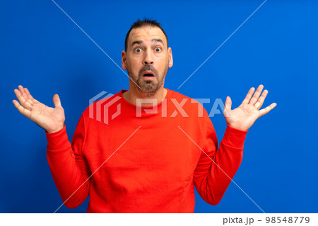 Amazed and excited latin man looking at camera with a shocked expression feeling shocked from advertising shopping promotion, amazing betting win standing isolated on a blue background Amazed and excited latin man looking at camera with a shocked expression feeling shocked from advertising shopping promotion, amazing betting win standing isolated on a blue background 98548779