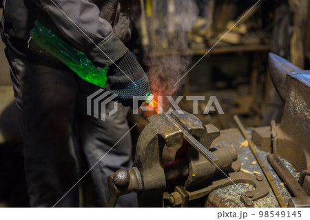 Blacksmith quenching hot iron part Blacksmith quenching hot iron part 98549145