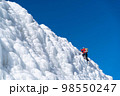 A climber in a red suit climbs an icy white mountain 98550247