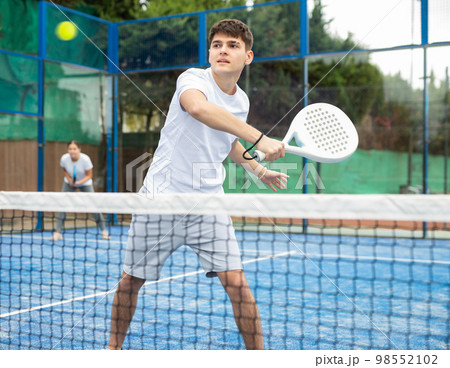 Male player ready to hits the ball while playing padel on hard court 98552102