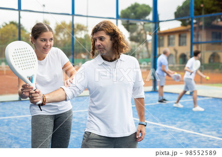 Girl teaching man to play padel tennis on outdoor court 98552589