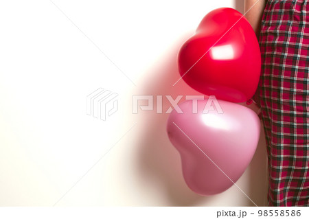 Inflatable helium balloons in the shape of a heart for Valentine's Day are held by a woman. Front view. 98558586