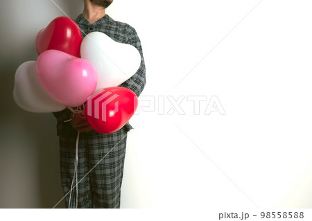 Inflatable helium balloons in the shape of a heart for Valentine's Day are held by a man. Front view. 98558588