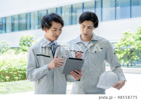 ビルの前でタブレットを見る若い作業員と現場監督の2人　撮影協力「LINK FOREST] 98558775