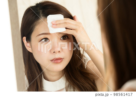 女性は鏡を見て、コットンで額を拭いている。 98561417