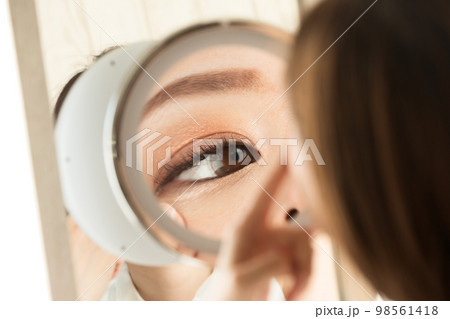 女性は鏡で目を見ている。 98561418
