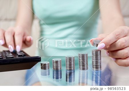Woman puts coins to a stack of coins and counting on a calculator Woman puts coins to a stack of coins and counting on a calculator 98563523