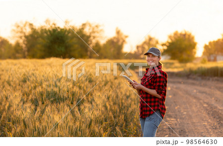 A woman farmer examines the field of cereals and sends data to the cloud from the tablet. A woman farmer examines the field of cereals and sends data to the cloud from the tablet. 98564630