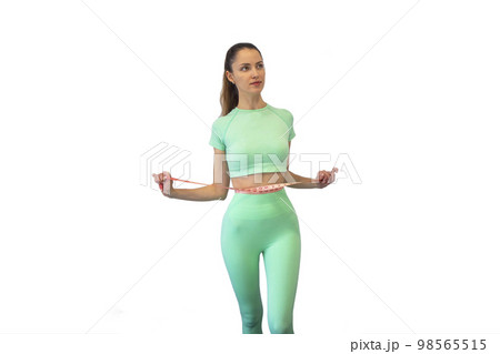 Young slim woman in turquoise spotwear measuring her waist with a tape measure, on isolated white background. Copy space. The concept of diet and weight loss. 98565515