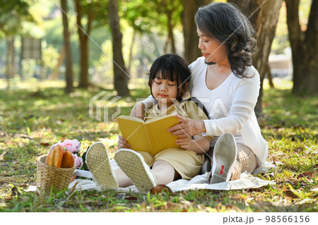Loving grandmother embracing little preschool granddaughter and reading reading fairy tale in sunny summer garden Loving grandmother embracing little preschool granddaughter and reading reading fairy tale in sunny summer garden 98566156