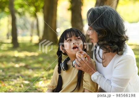 Smiling middle aged grandma and little preschooler child relaxing int he park. Family, generation and people concept Smiling middle aged grandma and little preschooler child relaxing int he park. Family, generation and people concept 98566198
