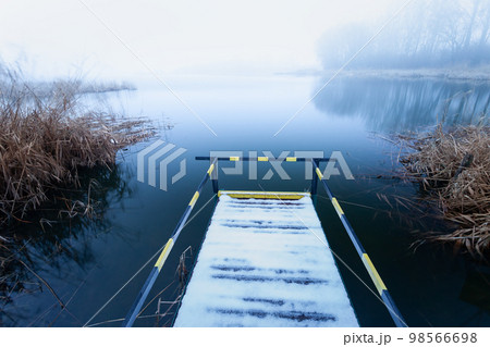 A pier with a handrail for disabled people on the shore of a lake on a foggy day 98566698