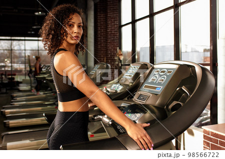 Fit smiling beautiful african american woman running on treadmill in gym Fit smiling beautiful african american woman running on treadmill in gym 98566722