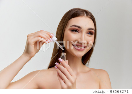 Portrait of young beautiful girl with healthy skin posing with face serum, toner over grey studio background. Concept of skincare and natural beauty Portrait of young beautiful girl with healthy skin posing with face serum, toner over grey studio background. Concept of skincare and natural beauty 98568271
