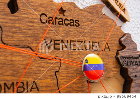 Venezuela flag on the pushpin with red thread showed the paths of movement or areas of influence in the global economy on the wooden map. Planning of traveling or logistic concept. Network connection Venezuela flag on the pushpin with red thread showed the paths of movement or areas of influence in the global economy on the wooden map. Planning of traveling or logistic concept. Network connection 98569454