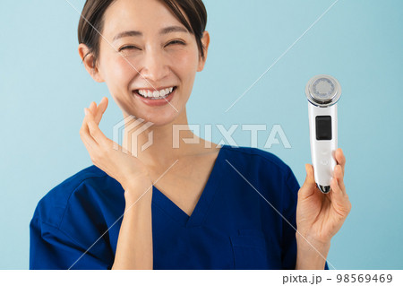 スクラブを着て美顔器の説明をしている若い女性 美容イメージ スクラブを着て美顔器の説明をしている若い女性 美容イメージ 98569469