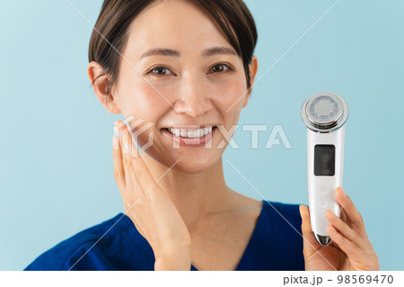 スクラブを着て美顔器の説明をしている若い女性　美容イメージ 98569470