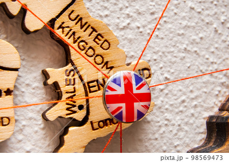 United Kindom flag on the pushpin with red thread showed the paths of movement or areas of influence in the global economy on the wooden map. Planning of traveling or logistic concept. Network United Kindom flag on the pushpin with red thread showed the paths of movement or areas of influence in the global economy on the wooden map. Planning of traveling or logistic concept. Network 98569473