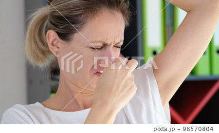 Worried woman with unhappy face checking smell of her armpit in office. 98570804