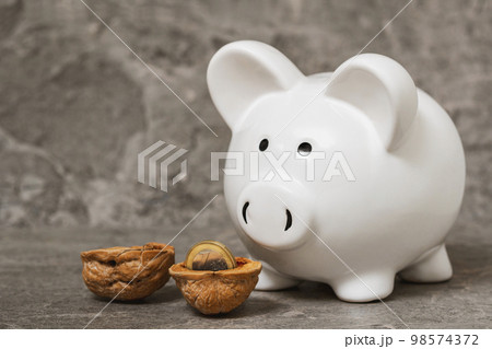 Piggy bank standing next to  cracked walnut shell and one euro coin 98574372