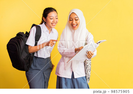 two high school girls opening books while carrying bags 98575905