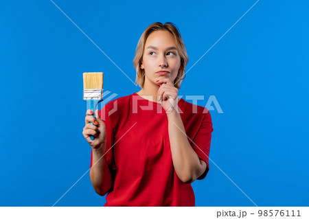 Young blonde woman artist with brush on blue background. Creative person. 98576111