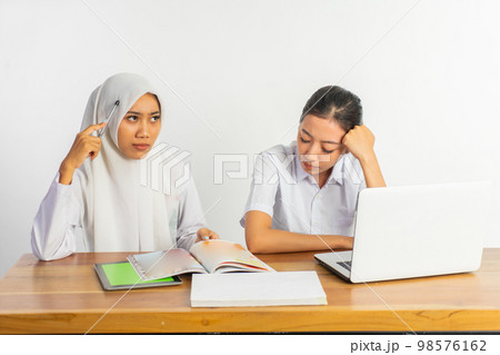 two high school girls sitting at desk in thinking pose two high school girls sitting at desk in thinking pose 98576162