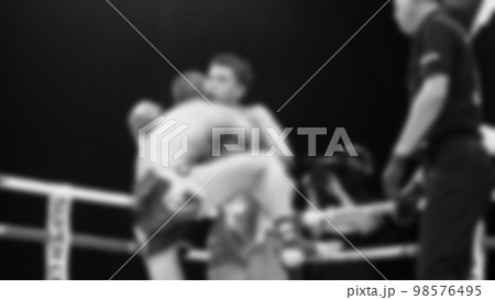Blurred images black and white photo style of Thai boxing or Muay Thai or Kickboxing which local and foriegn boxer are fighting on the ring at indoor stage as martial art sport. Muay Thai Kick boxing 98576495