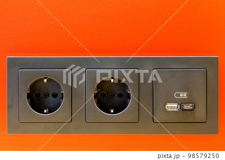 A black 220V, USB and USB C socket block is built into the orange wall surface A black 220V, USB and USB C socket block is built into the orange wall surface 98579250
