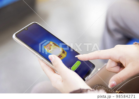 電車内でスマホゲームで課金してガチャをする若い女性手元 98584271