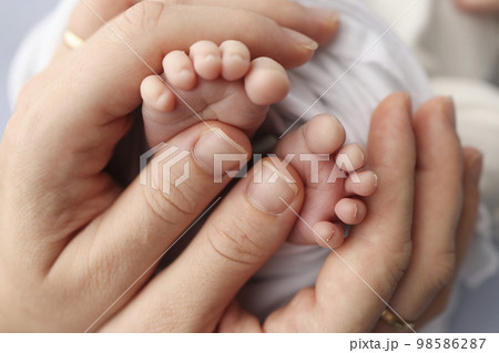Small feet of a newborn in the hands of parents. Loving palms of the hands of mother. Conceptual image of fatherhood. Close-up, selective focus. Professional photography a white background. Small feet of a newborn in the hands of parents. Loving palms of the hands of mother. Conceptual image of fatherhood. Close-up, selective focus. Professional photography a white background. 98586287