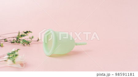 Green menstrual cup on a pink background next to dry plants 98591181