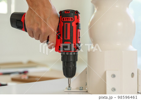 man assembling white table furniture at home using cordless screwdriver 98596461