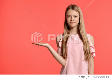 Studio portrait of a beautiful girl blonde teenager in a rosy t-shirt posing on pink background. Studio portrait of a beautiful girl blonde teenager in a rosy t-shirt posing on pink background. 98596634