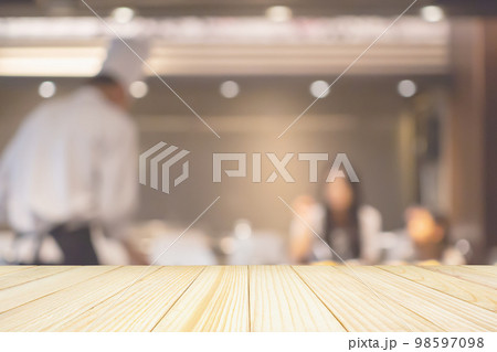 Empty wood table top with Chef cooking in restaurant kitchen abstract blurred defocused background Empty wood table top with Chef cooking in restaurant kitchen abstract blurred defocused background 98597098