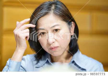 鏡を見て白髪に手をやる中年女性 98597773