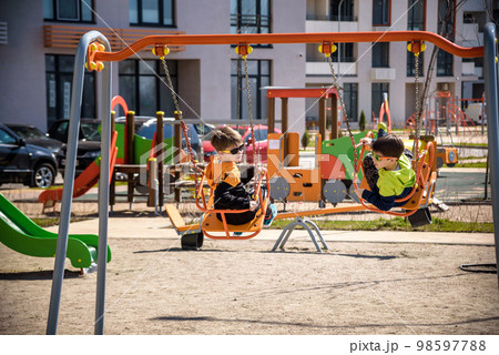 Two European boys swing on a swing in the summer holidays. Children have fun outdoors Two European boys swing on a swing in the summer holidays. Children have fun outdoors 98597788