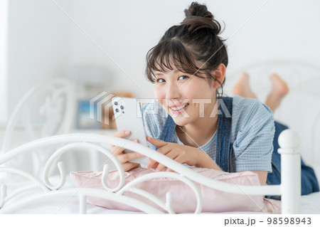 ベッドの上に横になってスマホを操作するz世代の女の子 ベッドの上に横になってスマホを操作するz世代の女の子 98598943