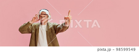 Young emotive man in casual clothes emotionally listening to music in headphones, posing over pink studio background. Concept of emotions, lifestyle Young emotive man in casual clothes emotionally listening to music in headphones, posing over pink studio background. Concept of emotions, lifestyle 98599549