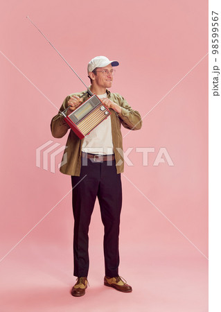 Listening to music, news. Young positive man posing with retro radio set over pink studio background. Concept of emotions, lifestyle 98599567