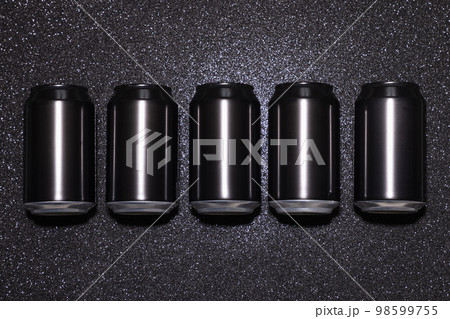 Blank black aluminum cans in a row on a black background with sparkles in hard light Blank black aluminum cans in a row on a black background with sparkles in hard light 98599755