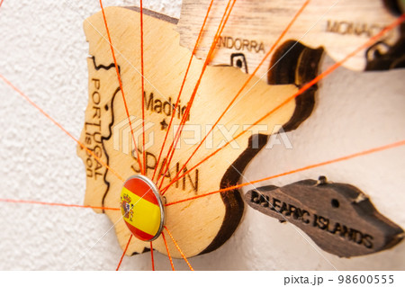 Spain flag on the pushpin with red thread showed the paths of movement or areas of influence in the global economy on the wooden map. Planning of traveling or logistic concept. Network connection.  98600555