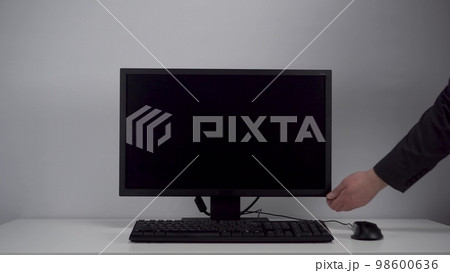 Turning on the monitor with a green screen. A man with his hand turns on the computer screen on the desktop in the office. Chroma key. 98600636