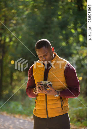 African american guy photographer taking picture with vintage camera on city green park - leisure activity, diversity and hobby concept 98603666