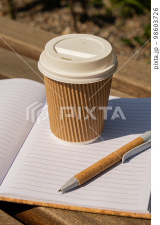 Eco recycling paper cup with coffee or tea on kraft paper with empty paper notebook on wooden bench. Concept of study work outdoors. Take away coffee to go. Copy space for text. Disposable Cardboard 98603726