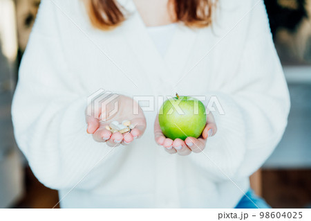 Female hands with green apple and different pills. Choose between natural, folk and traditional synthetic way of vitamins, health care. Diet modification, diabetes management, drugs alternative. Female hands with green apple and different pills. Choose between natural, folk and traditional synthetic way of vitamins, health care. Diet modification, diabetes management, drugs alternative. 98604025