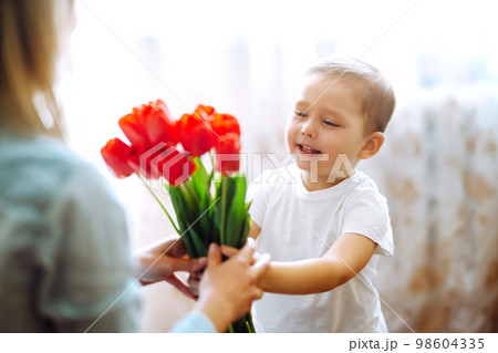 Little son congratulates mother, gives bouquet of flowers tulips. Happy mother's day. Family holiday 98604335