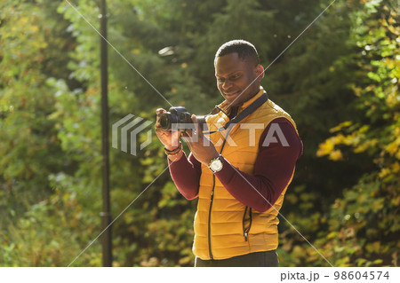 Close-up african american guy photographer taking picture with photo camera on city green park copy space and place for text - leisure activity, diversity and hobby concept Close-up african american guy photographer taking picture with photo camera on city green park copy space and place for text - leisure activity, diversity and hobby concept 98604574