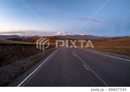 Morning highway to the snow-capped peaks. Autumn morning deserted highway. Beautiful asphalt freeway, motorway, highway through of caucasian landscape mountains hills. 98607595